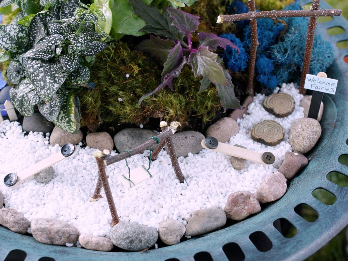 Miniature swing and slides on top of white pebbles surrounded by plants