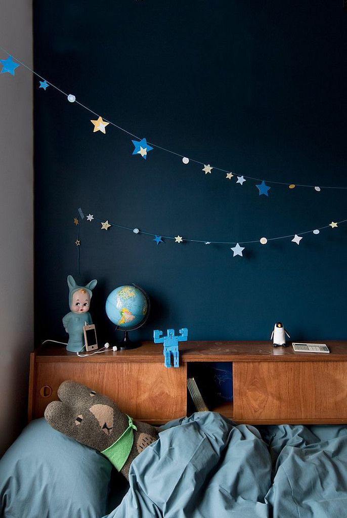Space children's room with a stuffed animal tucked in the comforter, flanked by star cut-outs hung from string.